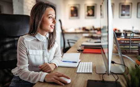 A brown haired woman sits in front of a computer with her hand on the mouse